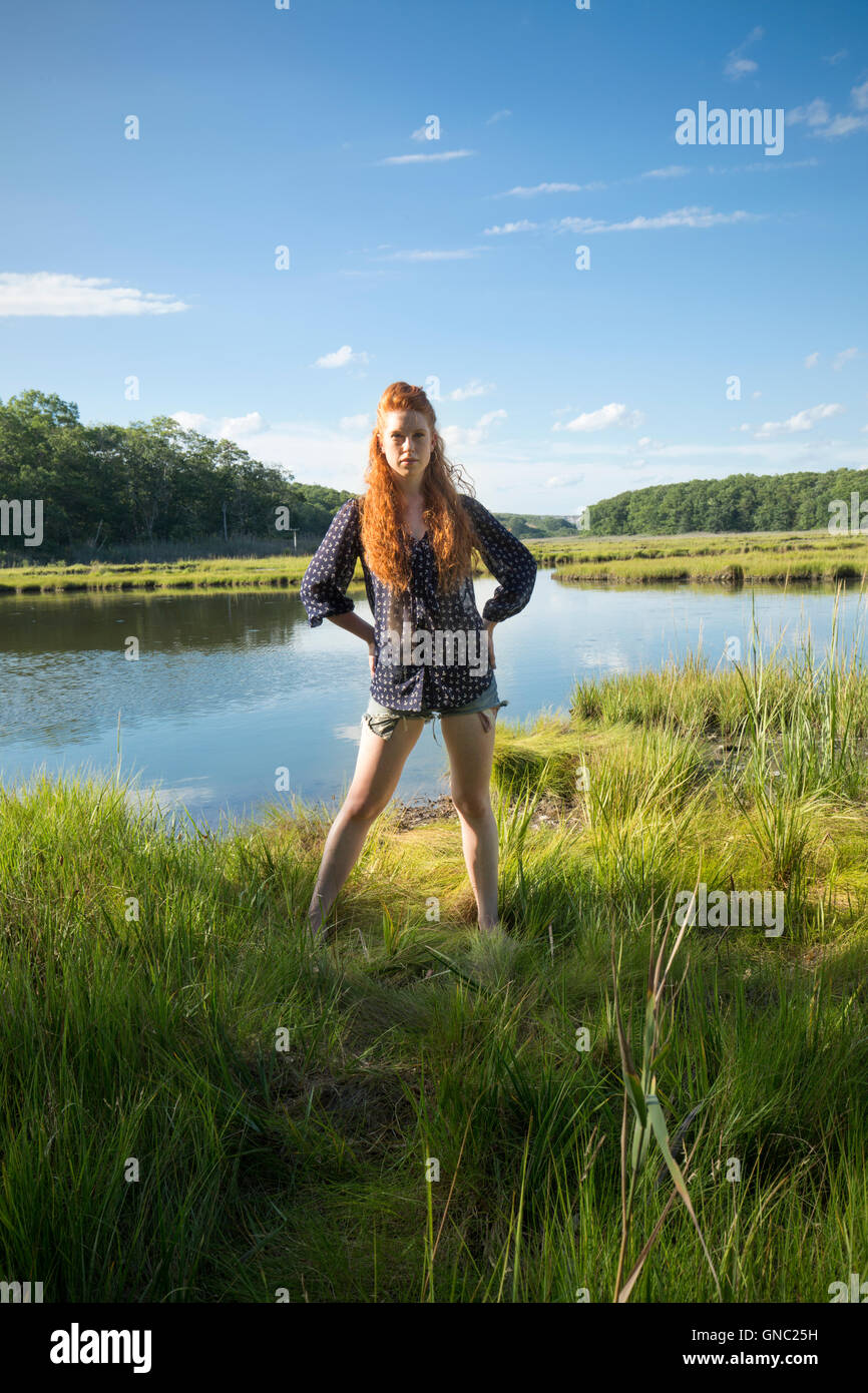 Junge Frau mit langen roten Haaren stehen auf der Hut in einem ruhigen Sumpf im Sommer trägt Shorts und ein t-Shirt. Stockfoto