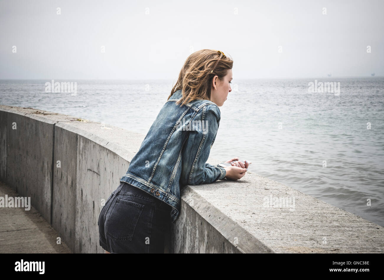 Junge Frau stützte sich auf Barriere, Santa Barbara Harbor, Kalifornien, USA Stockfoto
