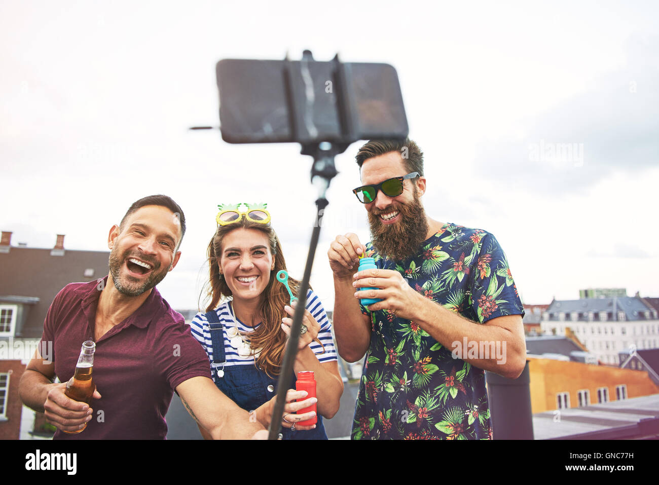 Drei feiern junge erwachsene Freunde im Sommer Bekleidung, die Bilder von sich selbst auf dem Dach beim Biertrinken und blasen Bubb Stockfoto