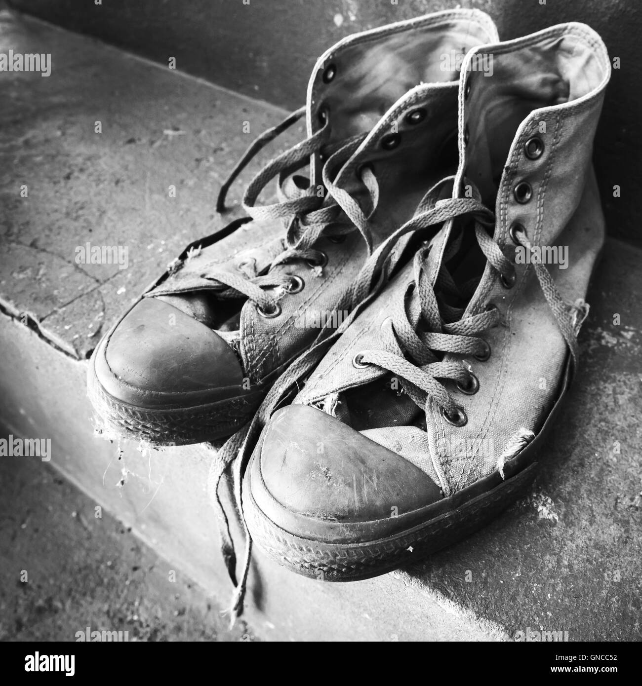 Paar alte Turnschuhe stehend auf Betontreppen. Schwarz / weiß quadratisch Foto mit selektiven Fokus Stockfoto