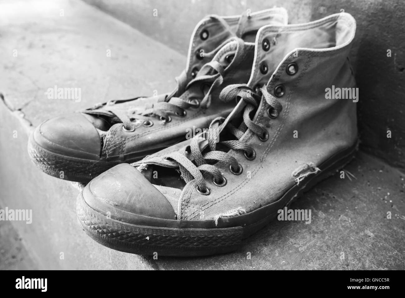 Paar alte Turnschuhe stehend auf Betontreppen. Schwarz / weiß Retro-stilisierte Foto Stockfoto