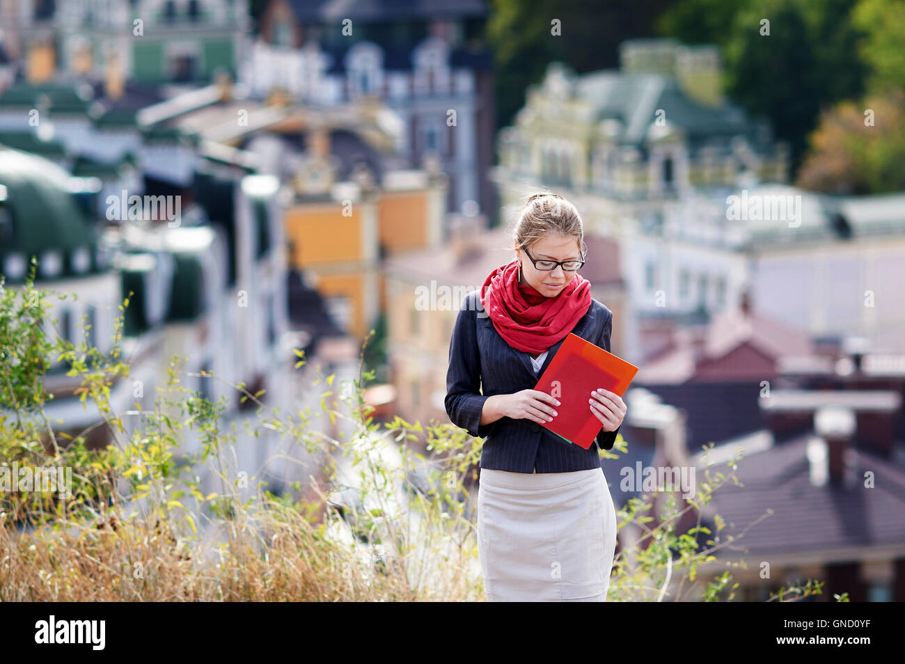 junge Frau in Gläsern mit roten Ordner auf Hintergrund der Stadt aufgehoben Stockfoto