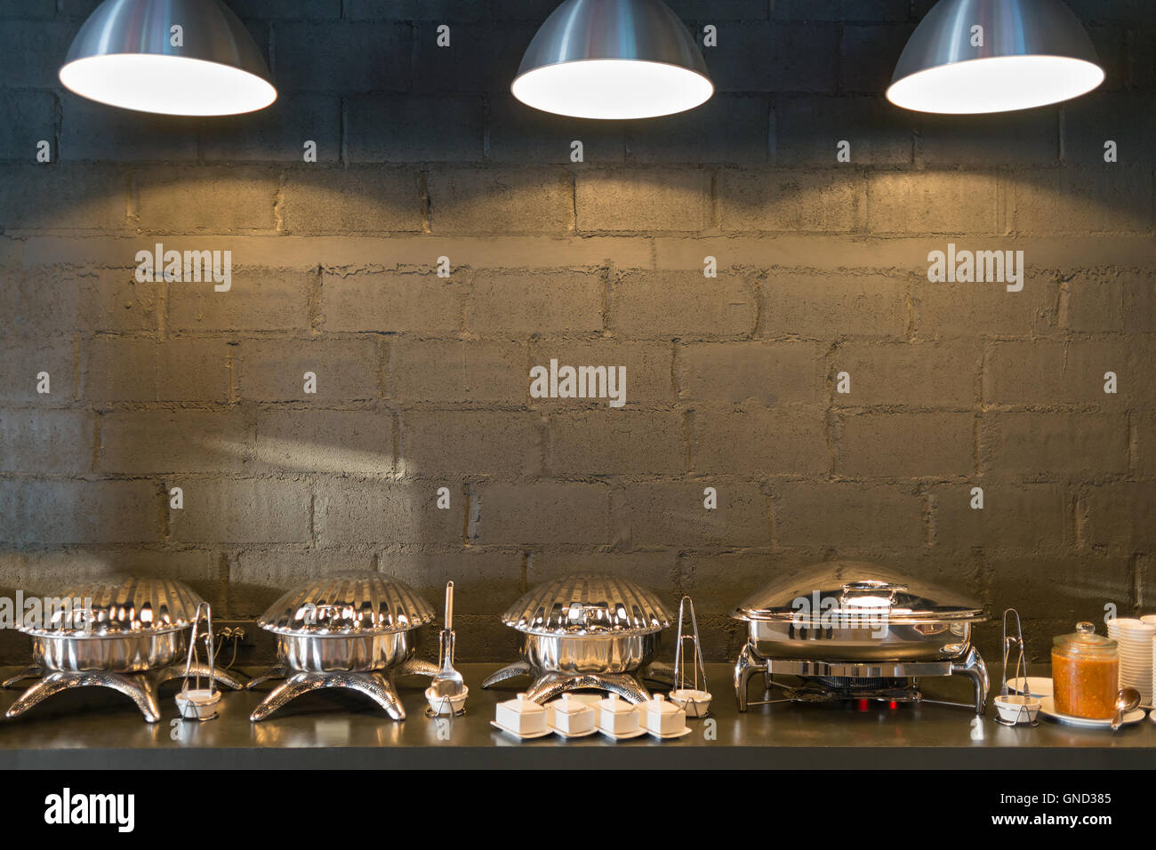 Büffet Linie Essen Container geformte Schalen mit drei Beleuchtung und dunklen Ziegel Wand Hintergrund. Stockfoto