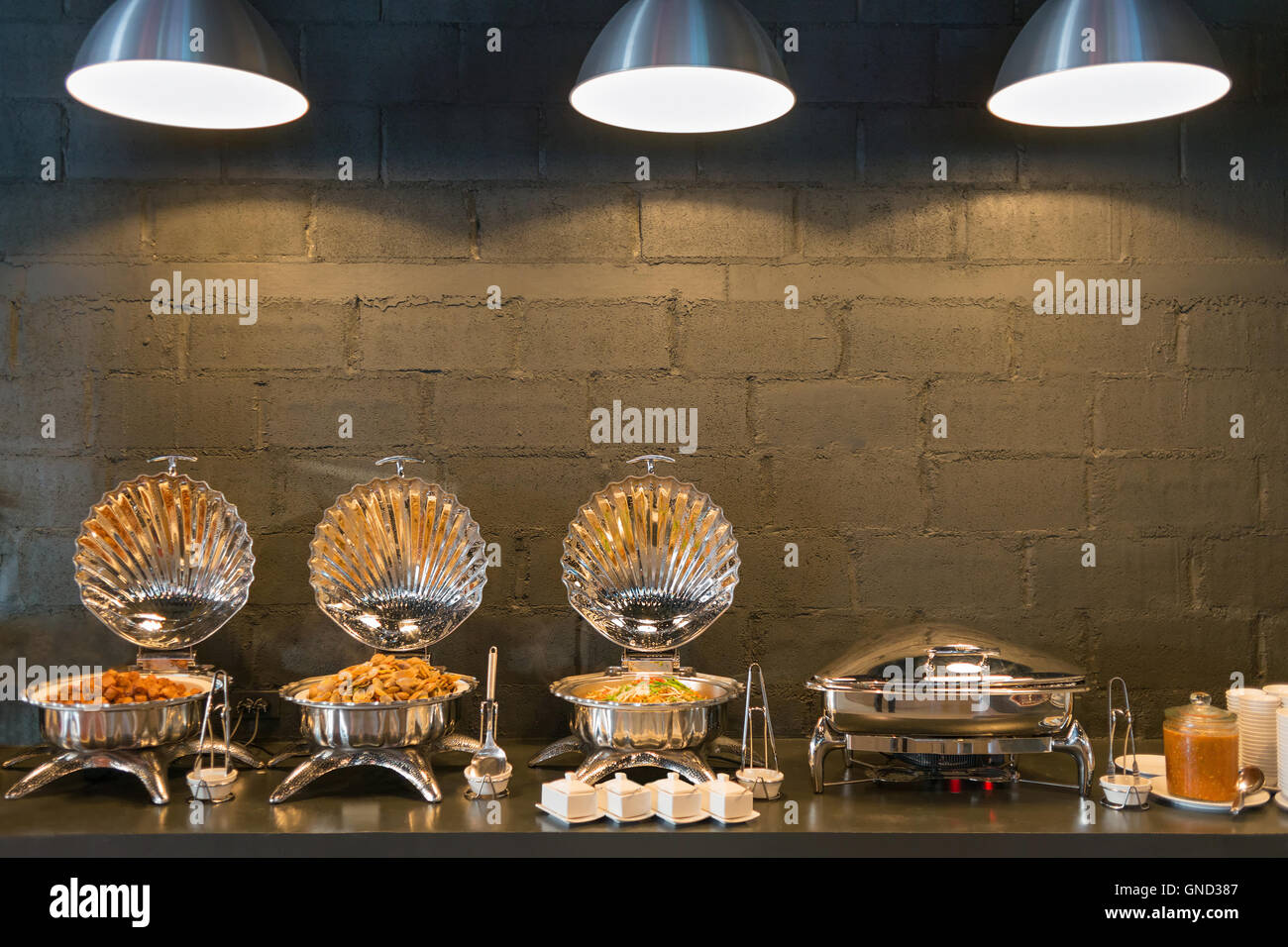 Büffet Linie Essen Container geformte Schalen mit drei Beleuchtung und dunklen Ziegel Wand Hintergrund. Stockfoto