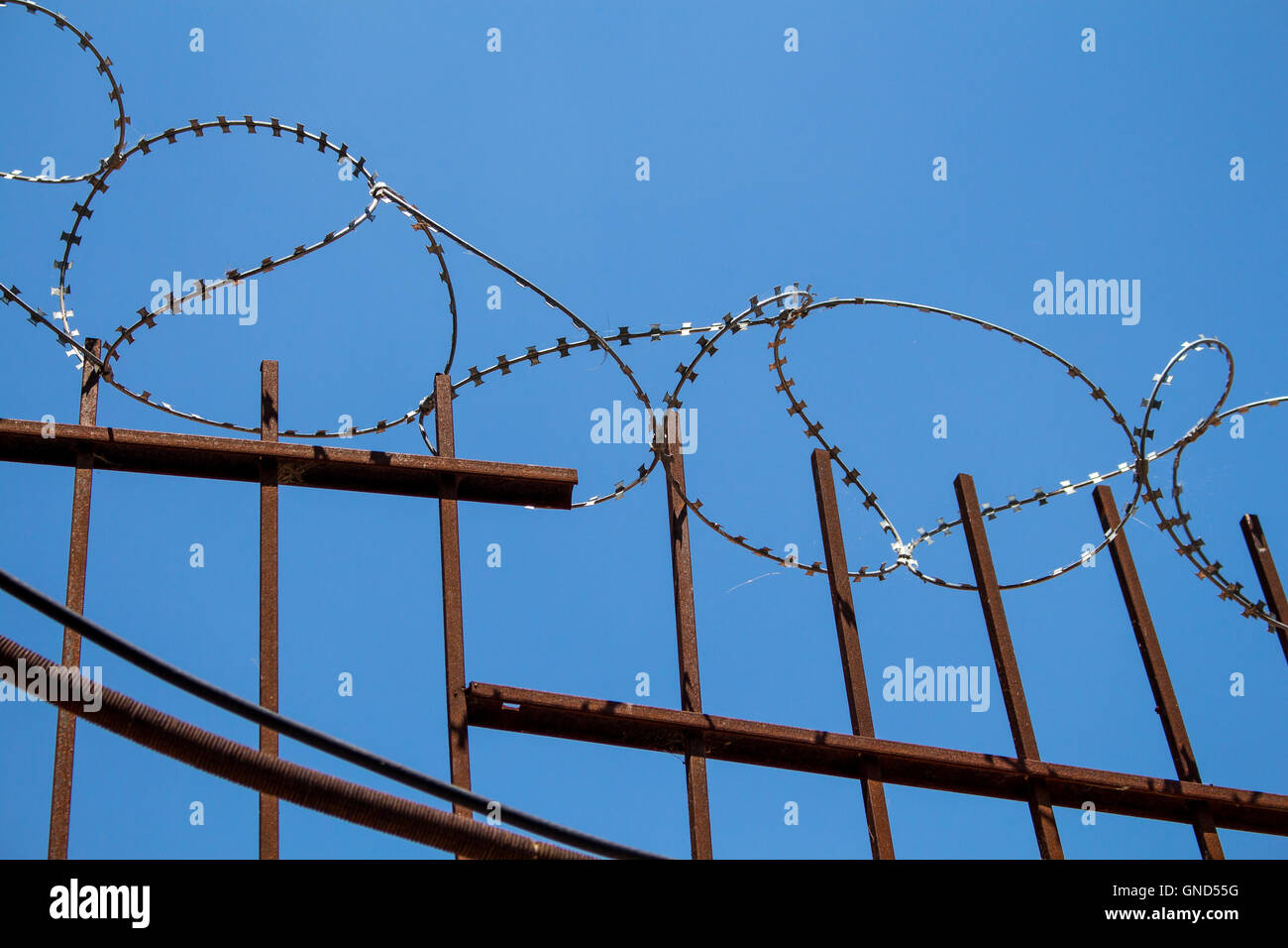 Aufgeklärte Stacheldraht auf der Oberseite einen Metallzaun. Strahlend blauer Himmel im Hintergrund. Stockfoto