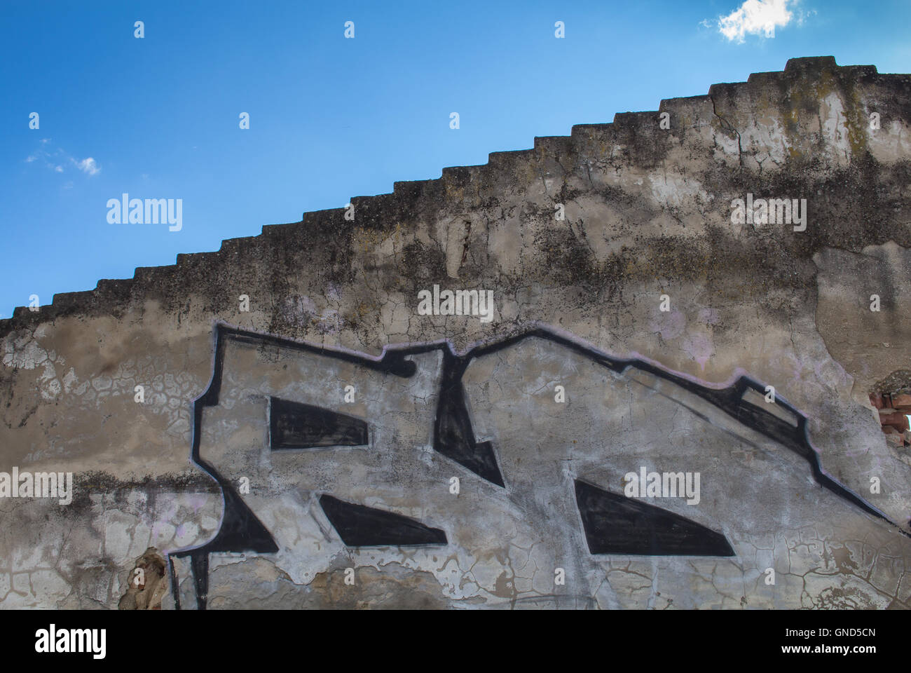 Kante des Daches und eine Wand mit beschädigten Fassade und ein Teil des Graffiti. Blauer Himmel mit kleinen weißen Wolken im Hintergrund. Stockfoto