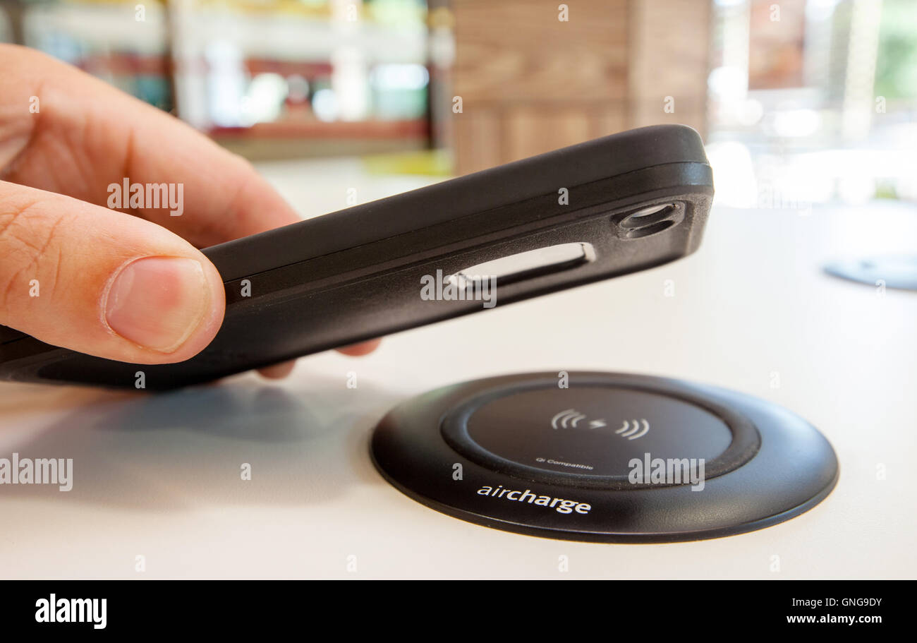 Ein Mann, der sein Handy auf ein Aircharge schnurloses Telefon Ladestation platzieren Stockfoto