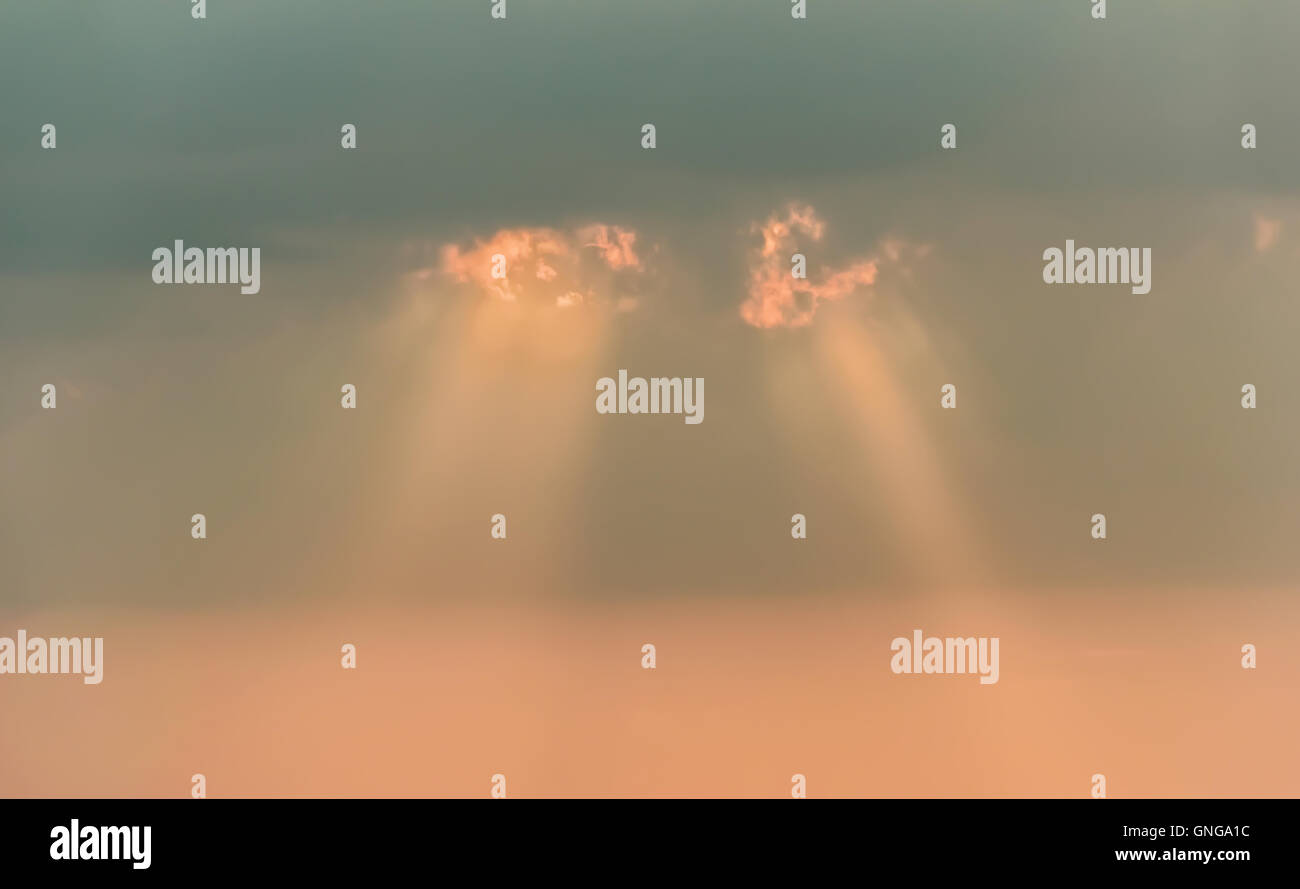 Lichtstrahlen durch graue und rosa Wolken im Himmel Stockfoto