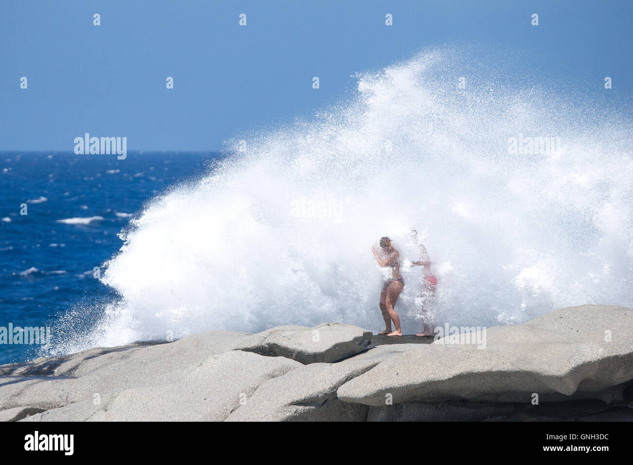 Zwei Frauen stehen auf Felsen schlagen durch große Welle, Korsika, Frankreich Stockfoto