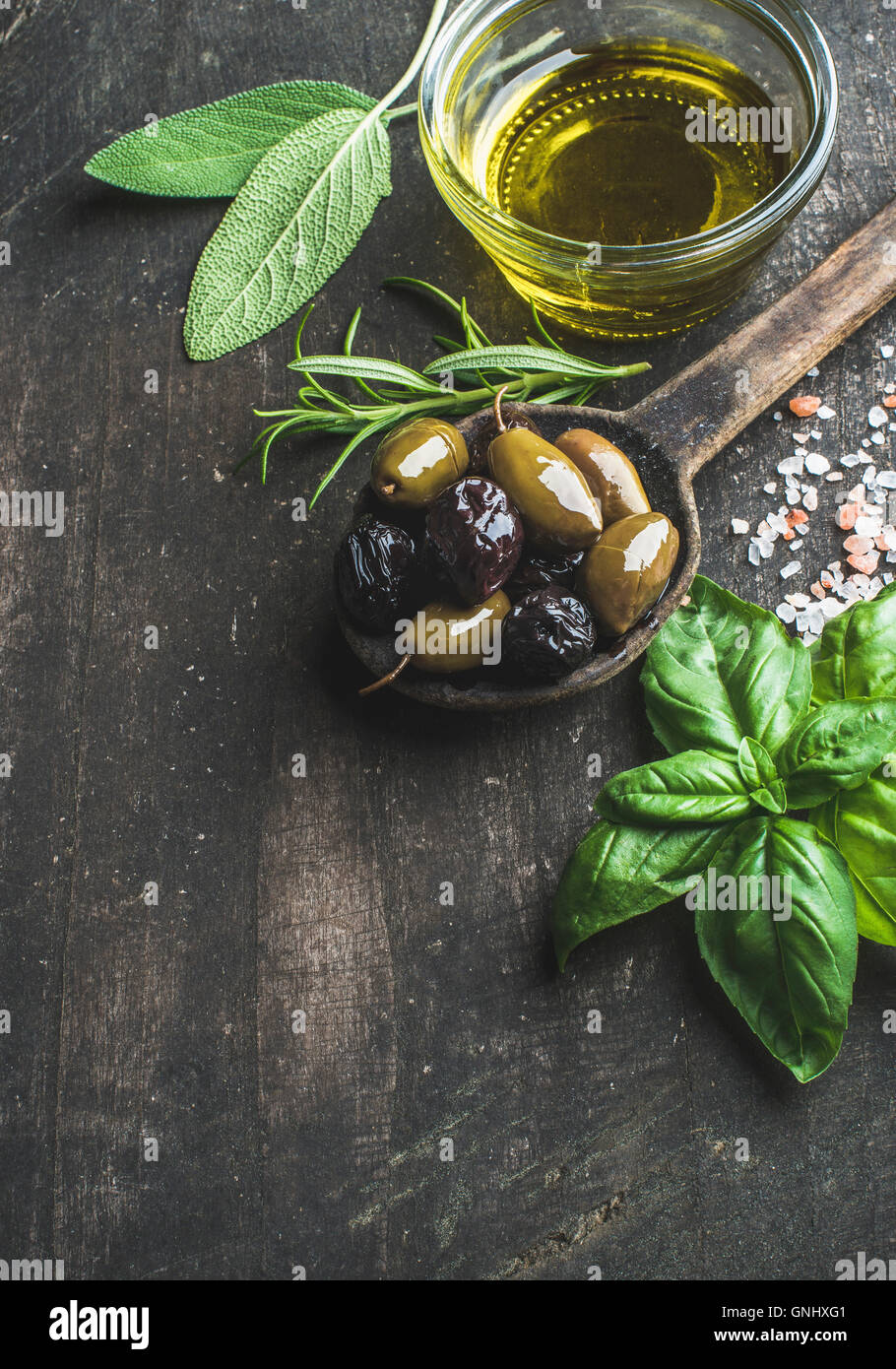 Grüne und schwarze mediterranen Oliven in alten Kochlöffel mit Olivenöl und Kräutern über rustikale Holz dunkel, Ansicht von oben, Stockfoto