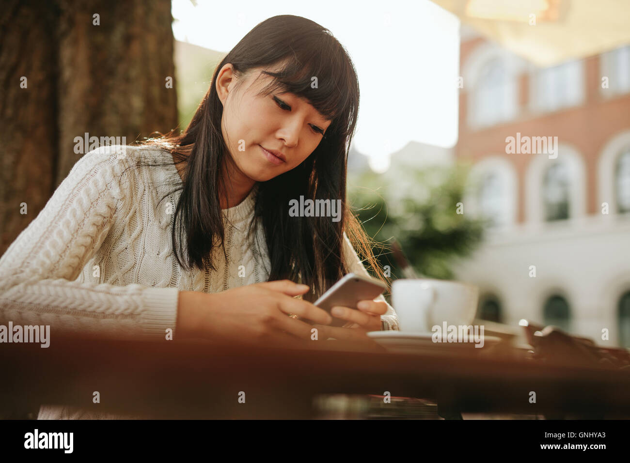 Chinesische Frau Textmitteilung auf smart Phone in einem Café zu schreiben. Bild junge Frau sitzt an einem Tisch mit einem Kaffee mit mobilen p Stockfoto
