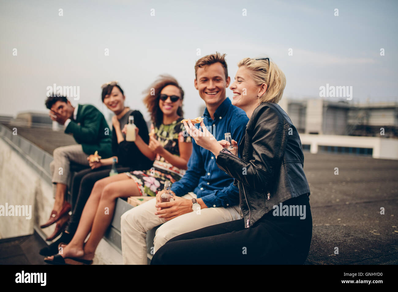 Aufnahme des jungen Menschen feiern auf der Terrasse. Gemischtrassig Freunde sitzen zusammen auf Dachterrasse, die Getränke und Essen. Stockfoto