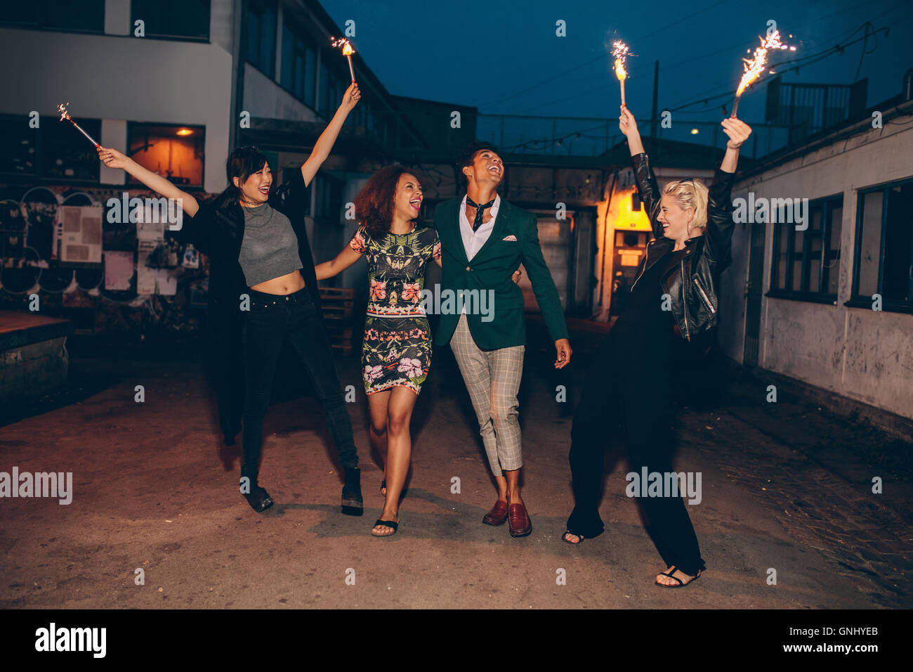 Begeistert junge Freunde gehen auf Stadtstraße in der Nacht mit einem Feuerwerk. Gruppe von Freunden genießen mit Wunderkerzen auf Straße in lösen Stockfoto