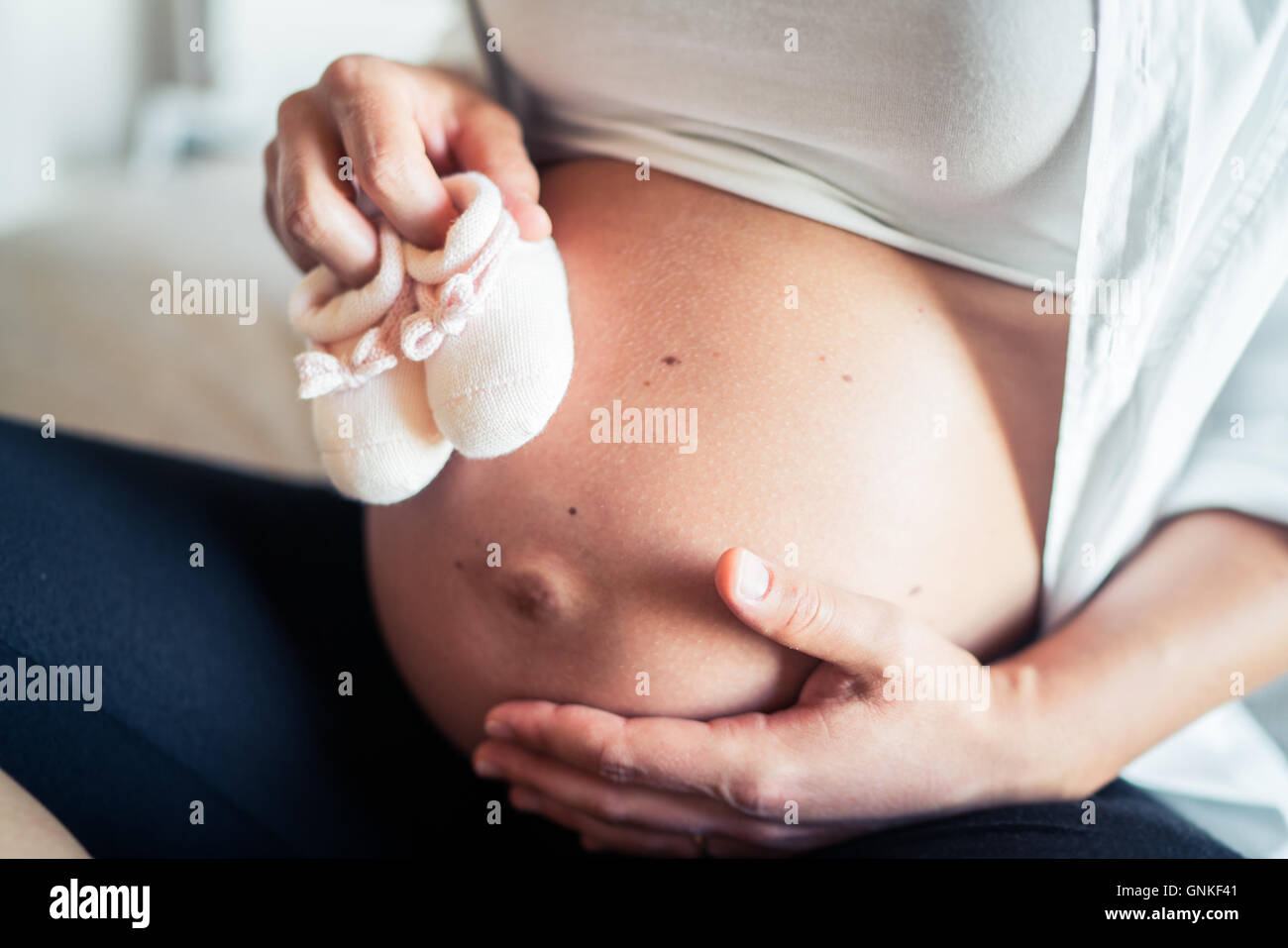 Schwangere Frau zeigt ihren Bauch und die weiße Wolle Schuhe des zukünftigen Kindes. Stockfoto