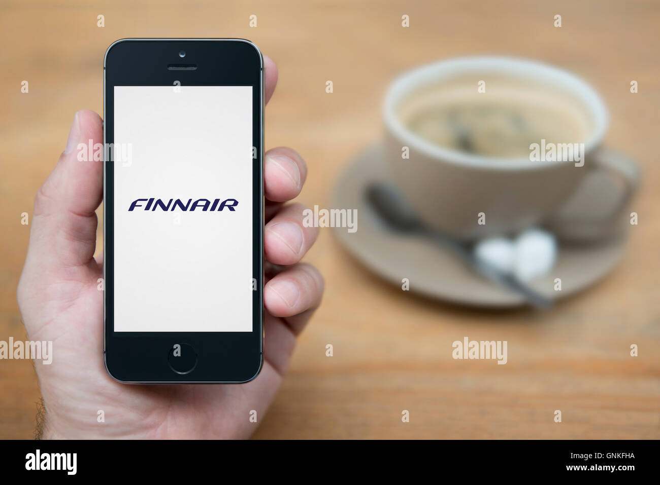 Ein Mann schaut auf seinem iPhone die Finnair-Logo anzeigt, während bei einer Tasse Kaffee (nur zur redaktionellen Verwendung) saß. Stockfoto