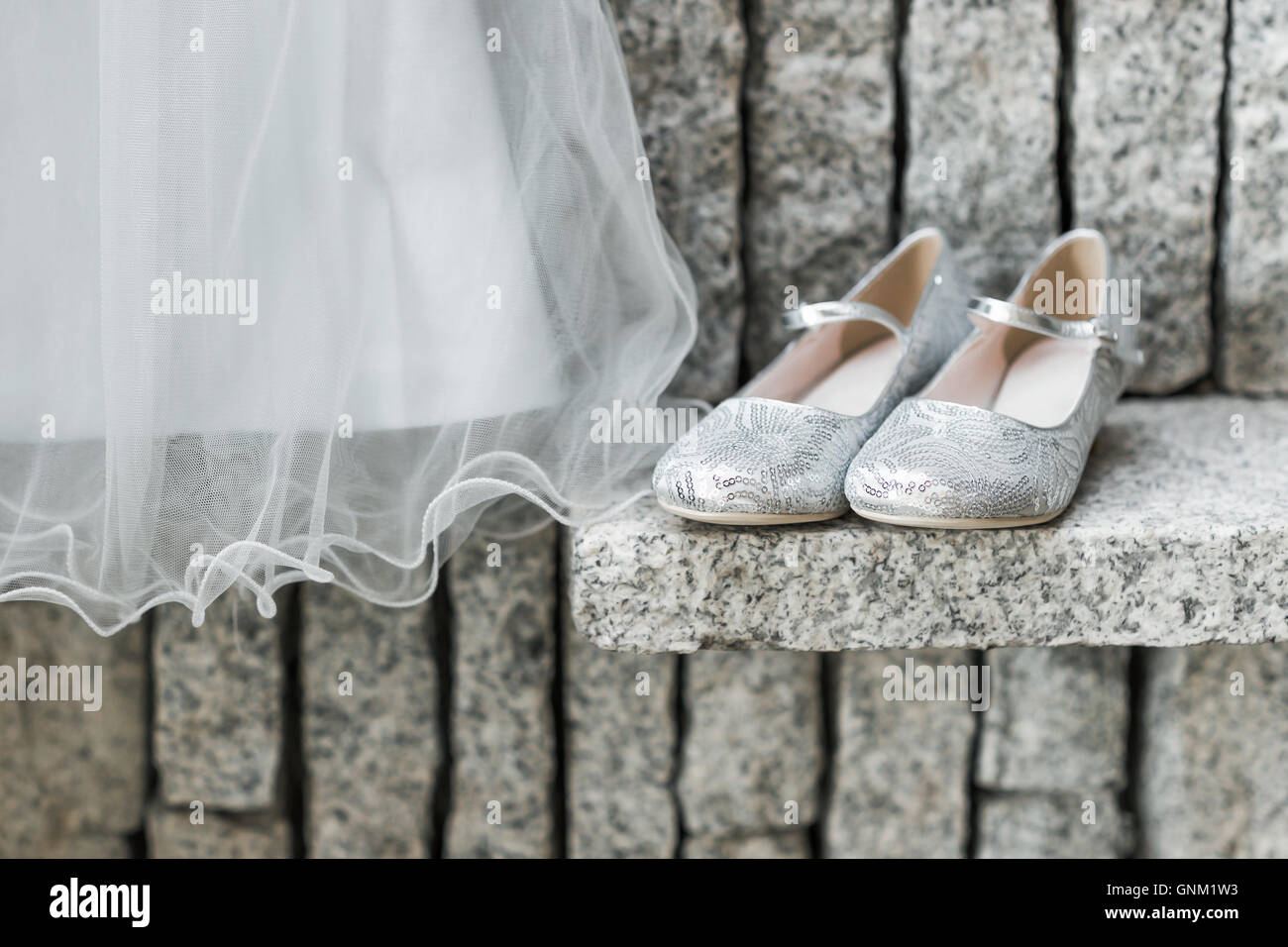 Ein Kind Hochzeit hängenden Kleid mit silbernen Schuhen neben auf Granit Hintergrund. Stockfoto