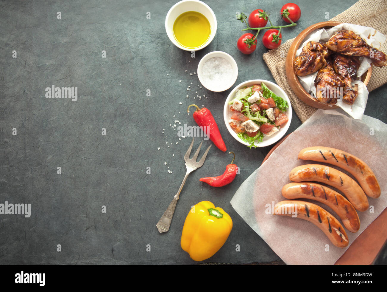 Auswahl an gegrilltem Fleisch wie Huhn und Würstchen mit Salat auf einem Holztisch Stockfoto