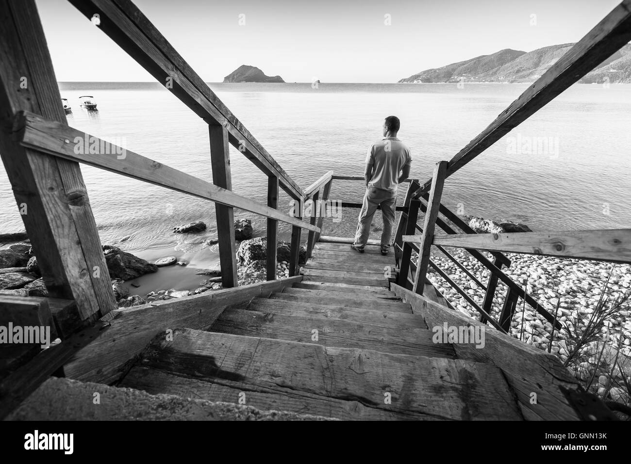 Junger Mann steht auf alte Holztreppe hinunter an die Küste des Meeres auf morgen, schwarz / weiß Foto Stockfoto