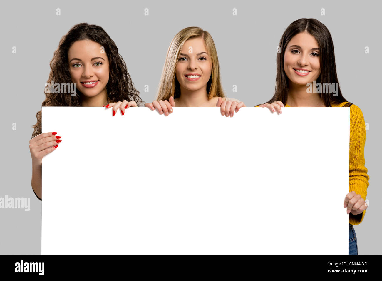 Studio-Porträt von drei Mädchen halten und zeigen etwas auf Karton Stockfoto