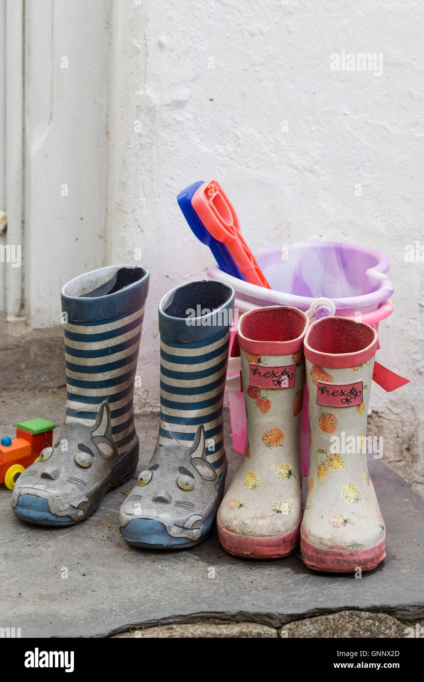 Kinder Gummistiefel und Eimer und Schaufel vor einer Haustür Stockfoto
