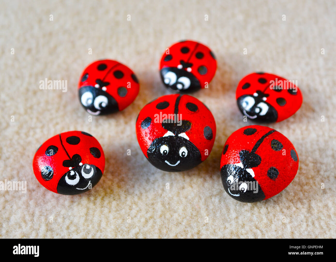 Familie von sechs niedliche Marienkäfer bemalt professionell in leuchtendem Rot mit schwarzen Flecken am Strand Kieselsteine in verschiedenen Größen. Stockfoto