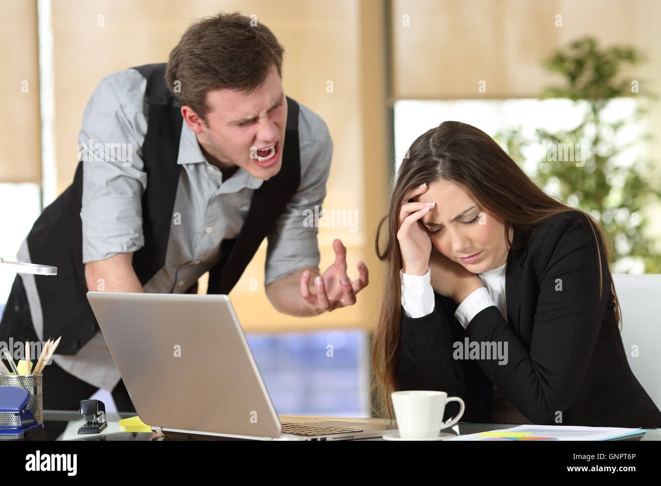 Mobbing mit Out of Control Chef schreien eine gestresste Mitarbeiter in einem Desktop im Büro Interieur Stockfoto