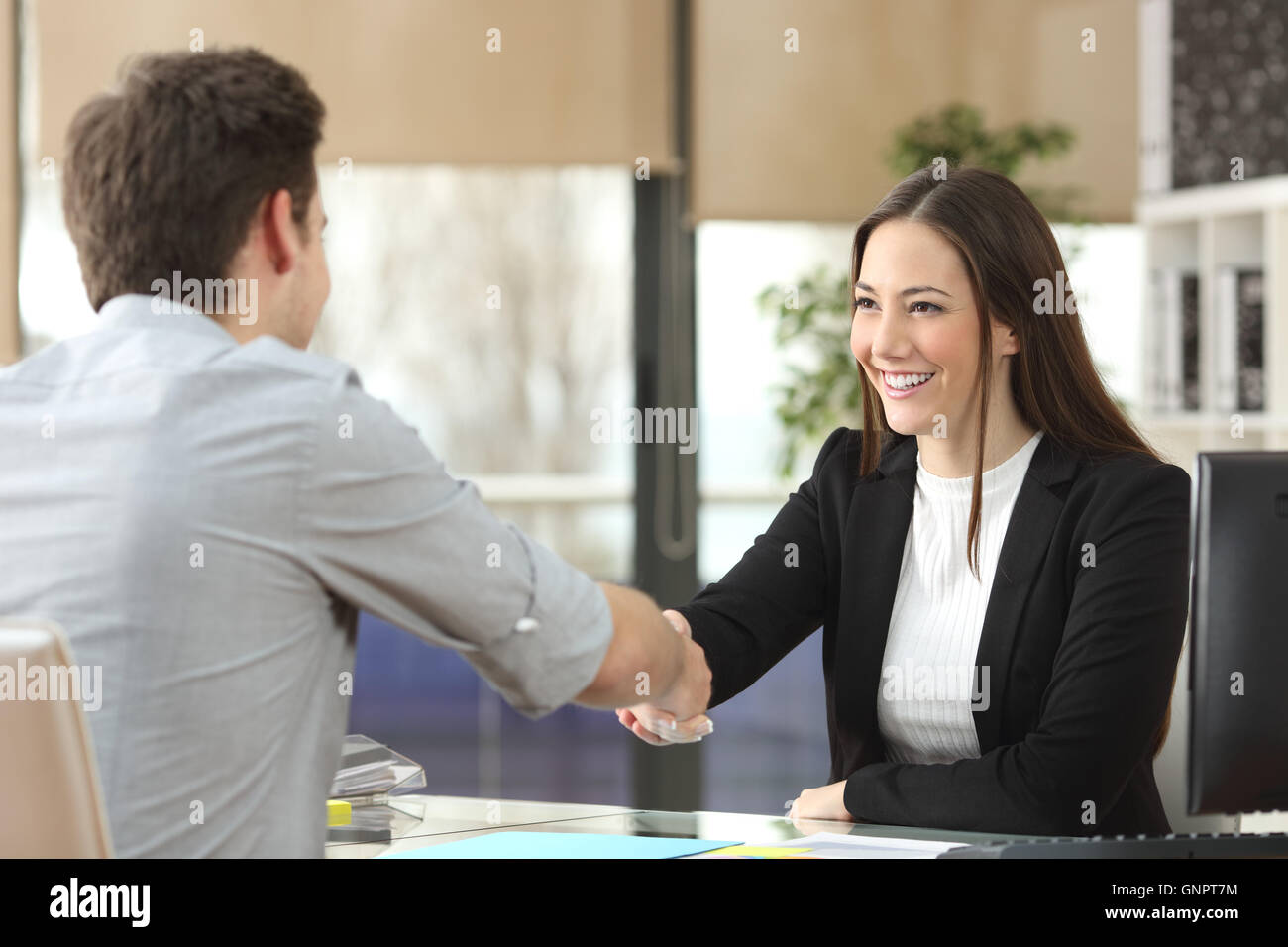 Glücklich Geschäftsfrau Handshaking mit Kunden ein Geschäft abgeschlossen in einem Büro Interieur mit Fenster im Hintergrund Stockfoto