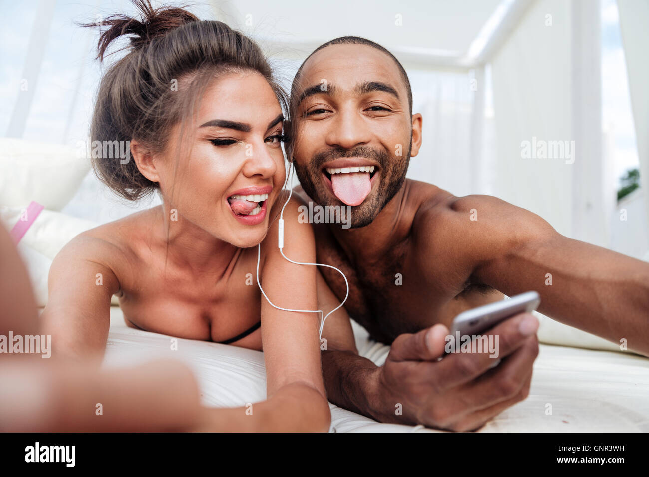 Fröhliche Brautpaar Selfie zu machen und zeigt Zungen beim hören von Musik am Strand Stockfoto