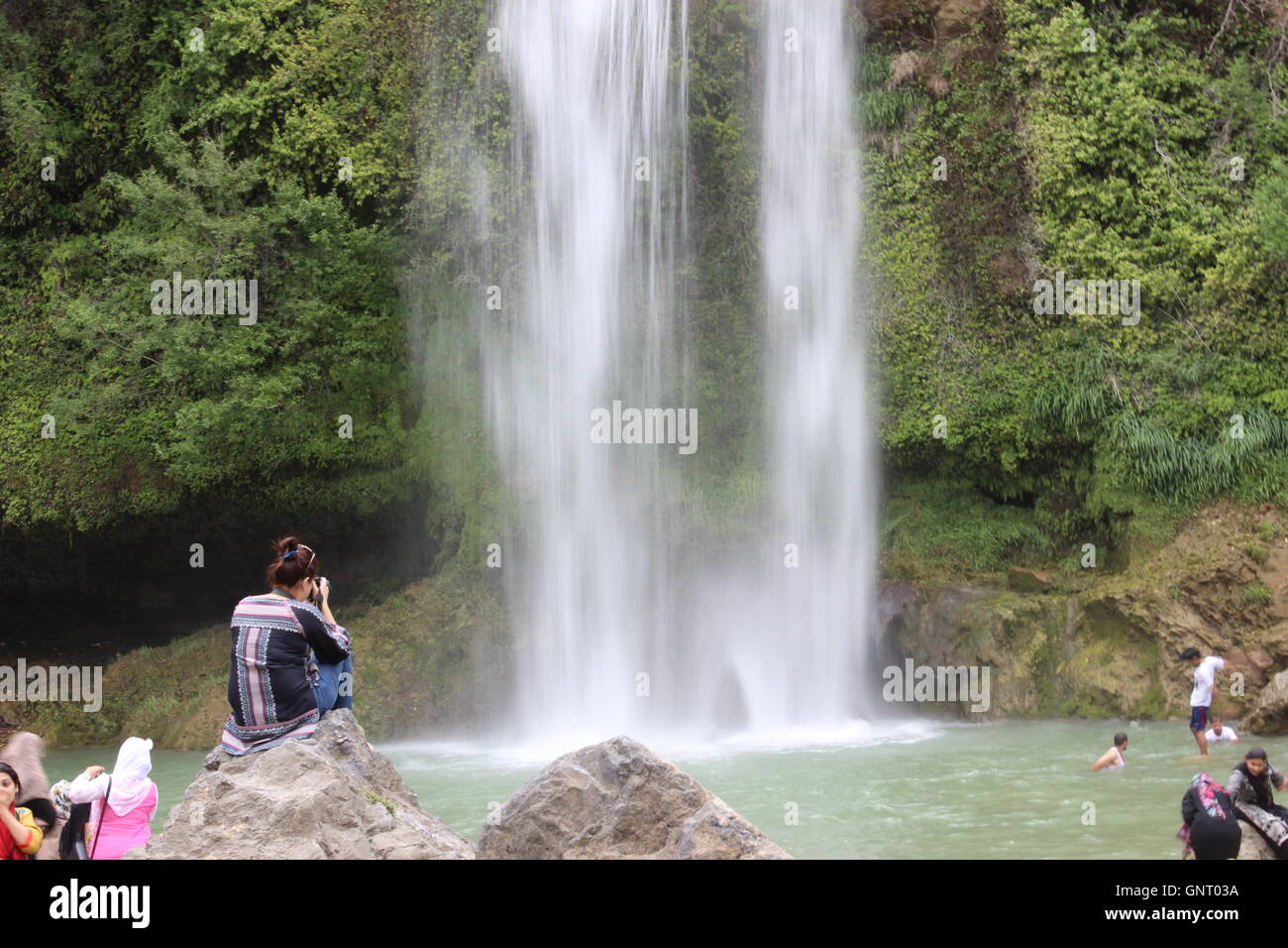 Ein slow-Shutter-Foto eines Wasserfalls, das Wasser, die Wangen hinunter und Schaffung eines verträumten Effekts. Eine Mädchen sitzt auf einem Felsen, die Erfassung der Szene Stockfoto