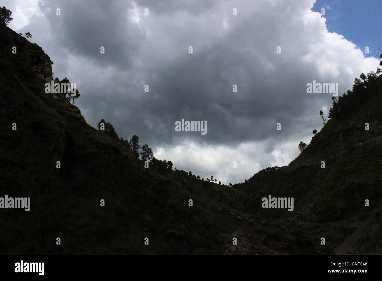 Ein Foto in hoher Apertur eines Tals des Berges (Silhouette) mit dunklen grauen Wolken im Hintergrund Stockfoto