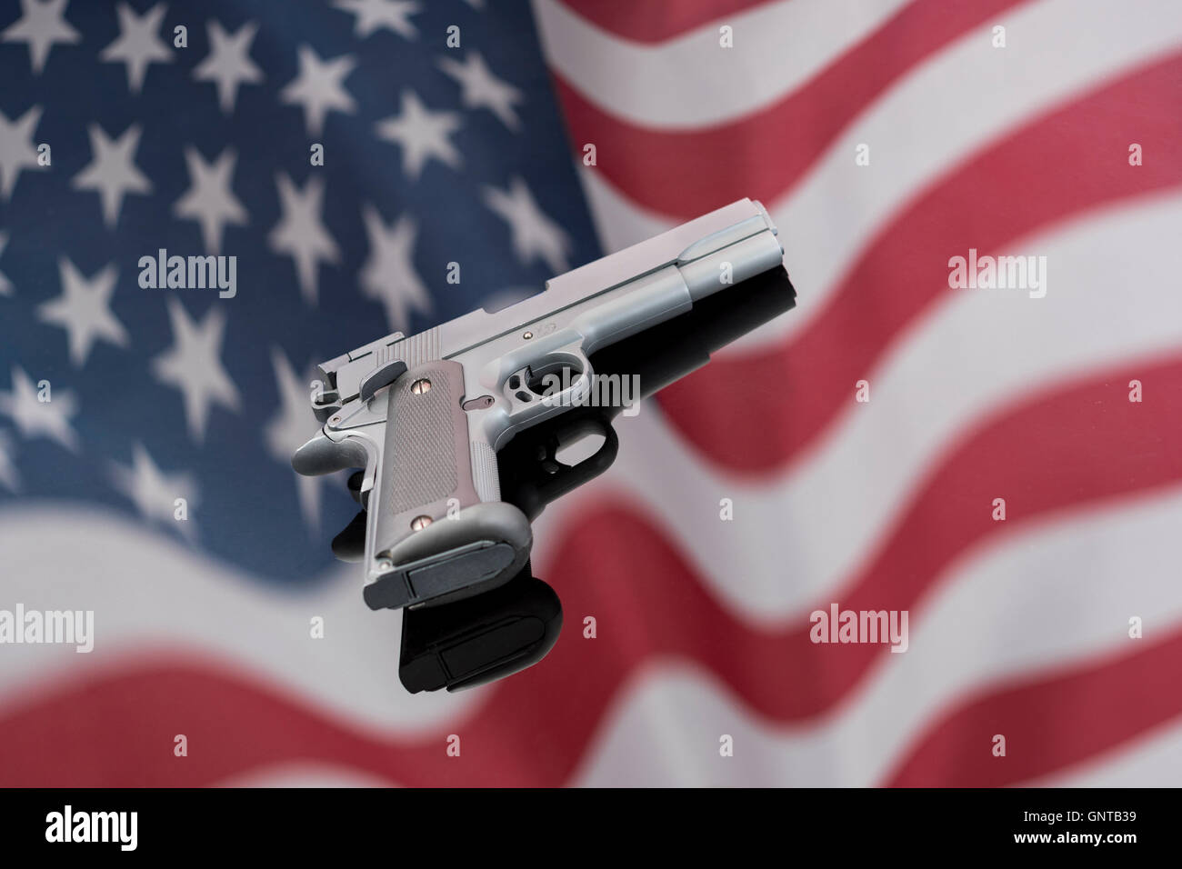 Replica Colt 1911A gegen Spiegelung der US-Flagge/Stars & Stripes - für Waffenkontrolle, US-Waffengesetze, Waffen, Verbrechenskonzept, Chicagoer Waffen, Gangs Waffen. Stockfoto