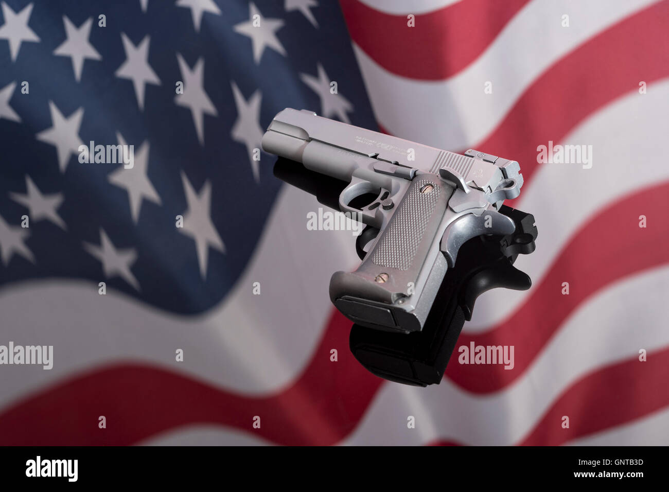 Replica Colt 1911A gegen Spiegelung der US-Flagge/Stars & Stripes - für Waffenkontrolle, US-Waffengesetze, Waffen, Verbrechenskonzept, Chicagoer Waffen, Gangs Waffen. Stockfoto