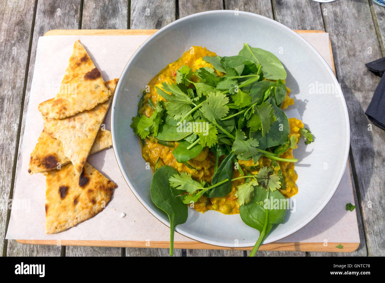 Café Mittagessen asiatisches Gemüse-Curry mit frischem Koriander und Baby-Blattspinat und Fladenbrot serviert. Stockfoto