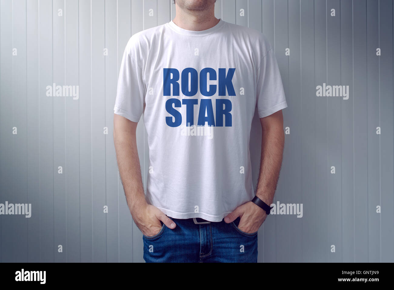 Lässige Männchen trägt T-shirt mit Rockstar Titel Mann in Jeans an die Wand gelehnt Stockfoto