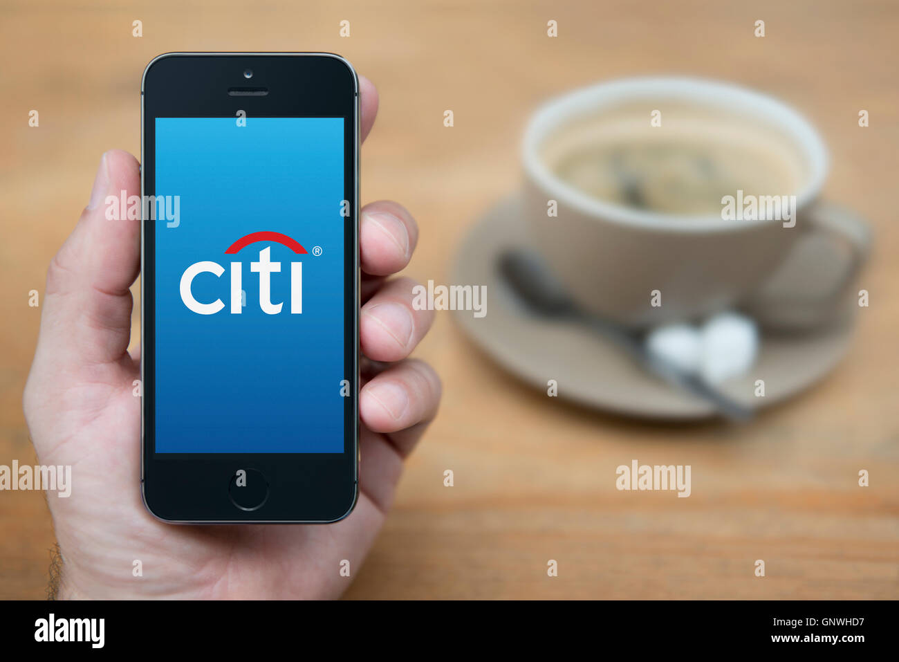 Ein Mann schaut auf seinem iPhone die Citi-Bank-Logo anzeigt, während bei einer Tasse Kaffee (nur zur redaktionellen Verwendung) saß. Stockfoto