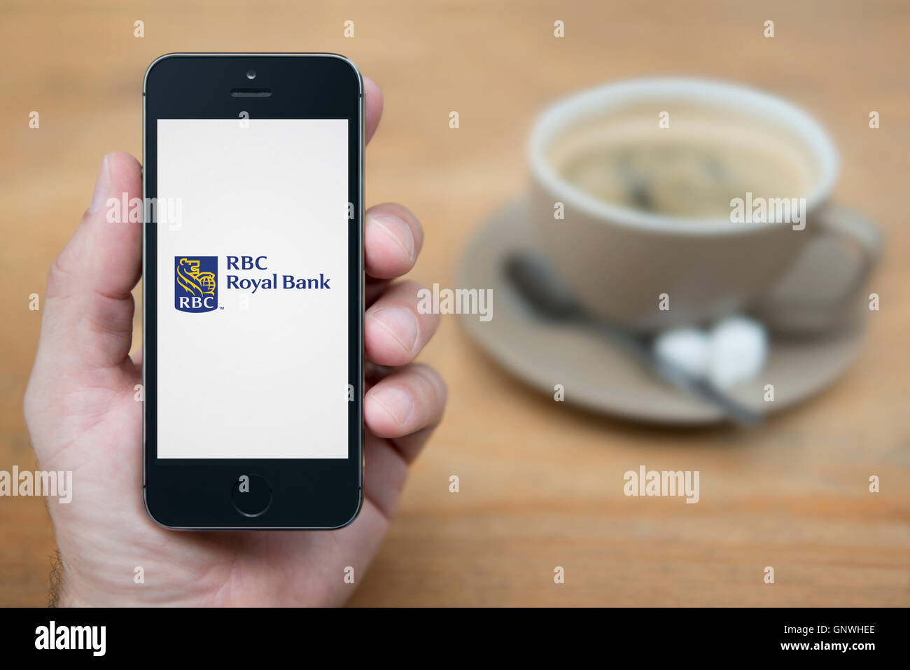 Ein Mann schaut auf seinem iPhone die RBC Royal Bank-Logo anzeigt, während bei einer Tasse Kaffee (nur zur redaktionellen Verwendung) saß. Stockfoto