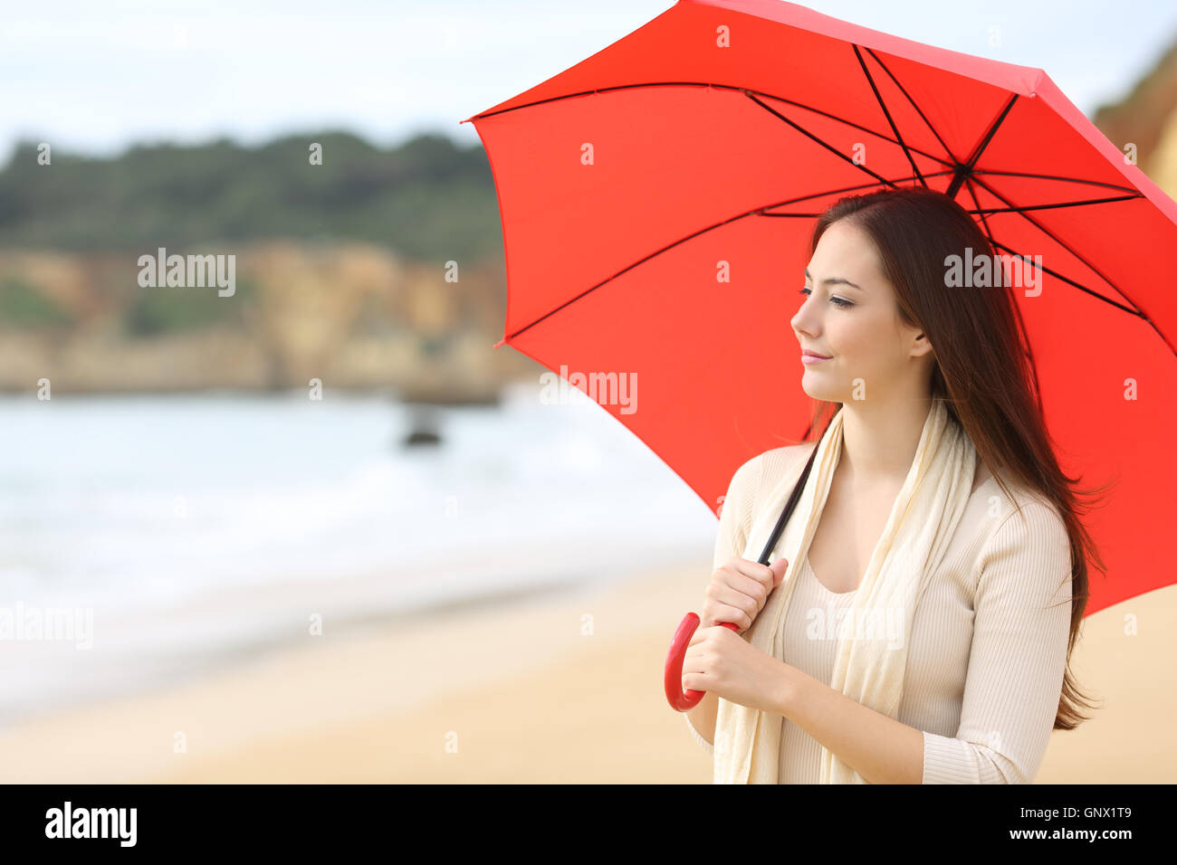 Porträt einer Sehnsucht Frau denken und der Blick auf Horizont unter einem roten Sonnenschirm am Strand mit dem Meer im Hintergrund Stockfoto