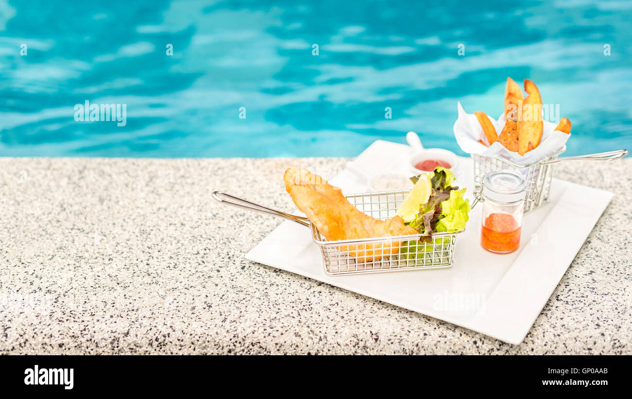 Fish &amp; Chips in weiße quadratische Platte mit verziert, am Pool. Textfreiraum. Stockfoto