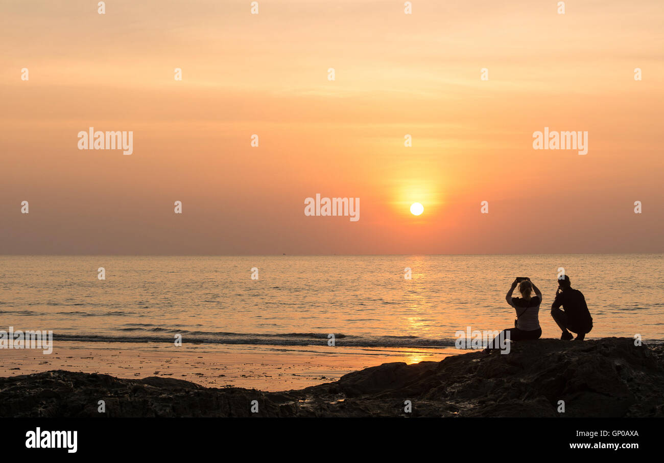 Seascape, erfasst Silhouette Paare auf Felsen sitzend ihr Gedächtnis bei Sonnenuntergang. Stockfoto