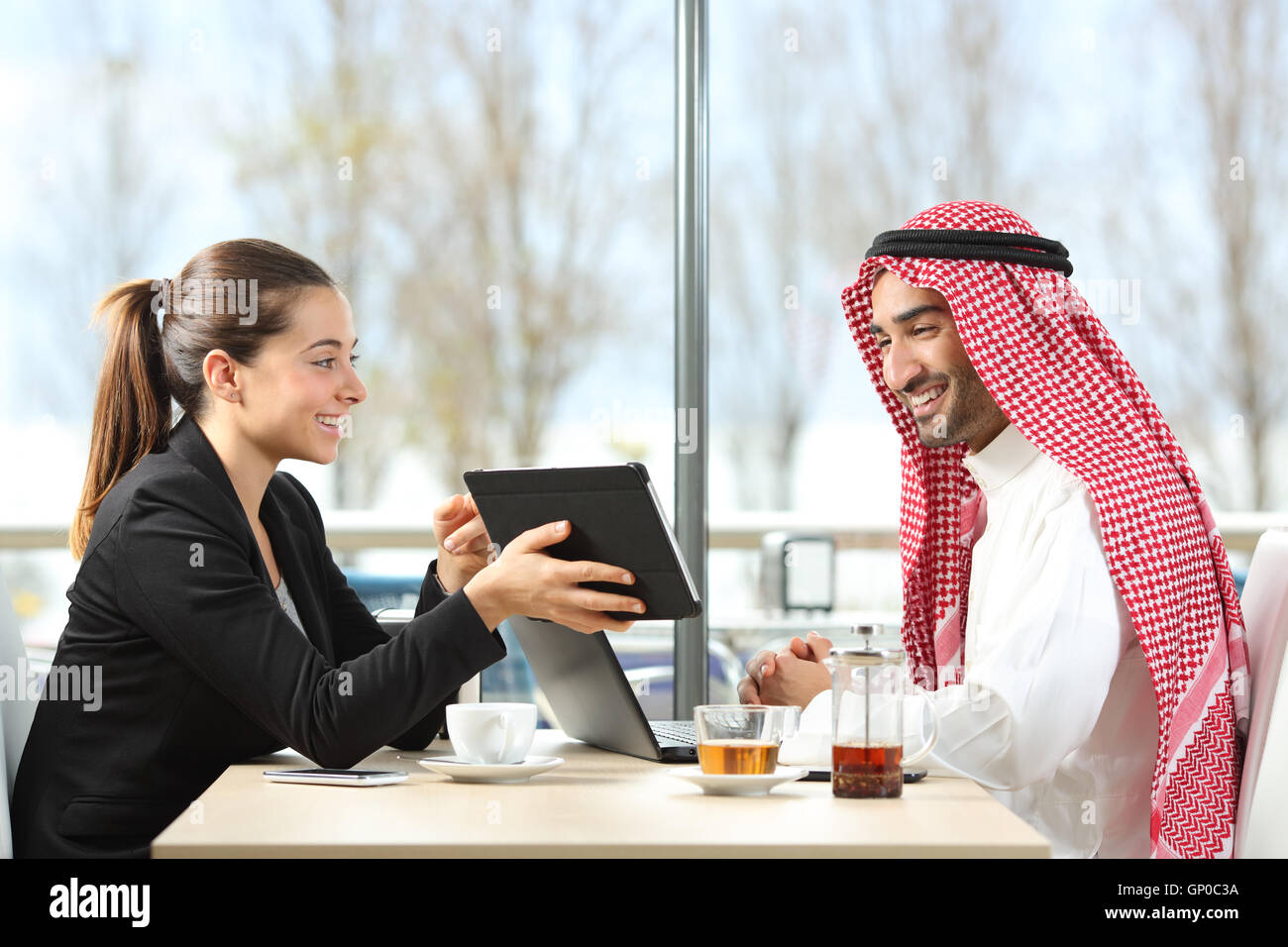 Geschäftsfrau oder Verkäuferin arbeitet mit einem arabischen Mann zeigt Produkte in einer Tablette in einem Coffee-shop Stockfoto