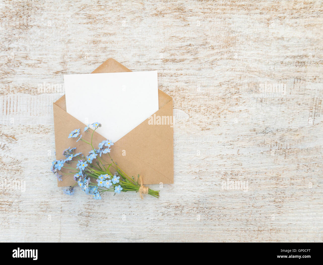 Braunen Papierumschlag mit weiße leere Karte und blaue Vergissmeinnicht Blumenstrauß gebunden mit Jute Seil auf die rustikale weiße Farbe Stockfoto