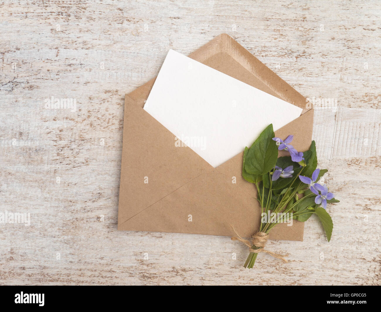 Braunen Papierumschlag mit weiße leere Karte und wilde Viola Blumenstrauß gebunden mit Jute Seil auf dem rustikalen weißen Hintergrund Stockfoto