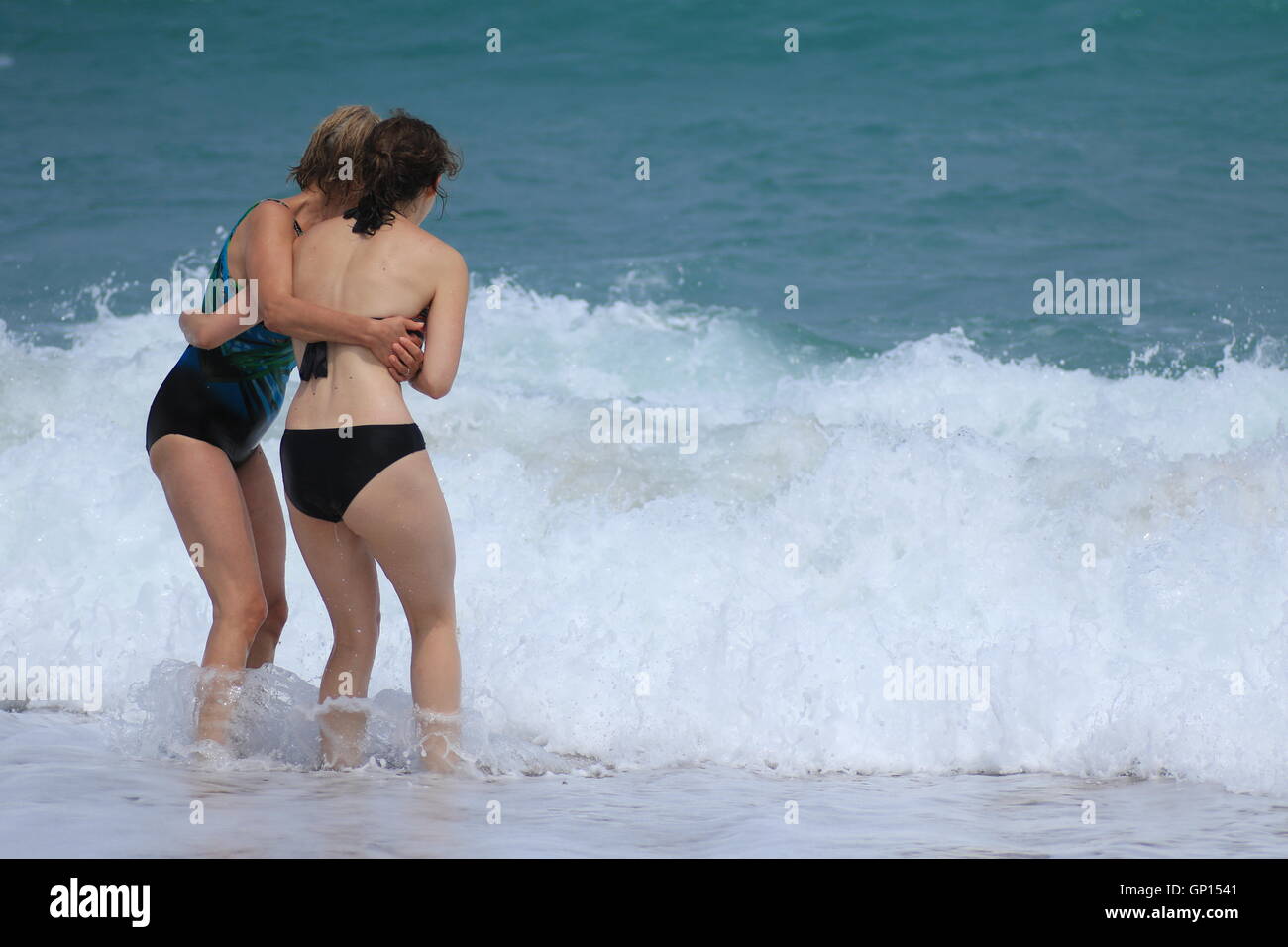 Frauen halten einander gegen ankommenden Wellen. Stockfoto
