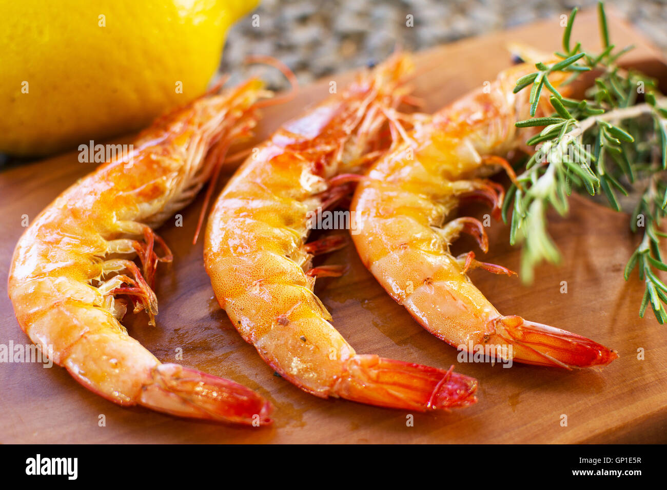 Gegrillte Garnelen auf einer hölzernen Platte serviert mit Zitrone und Rosmarin. Drei gegrillte Garnelen gewürzt Nahaufnahme. Stockfoto