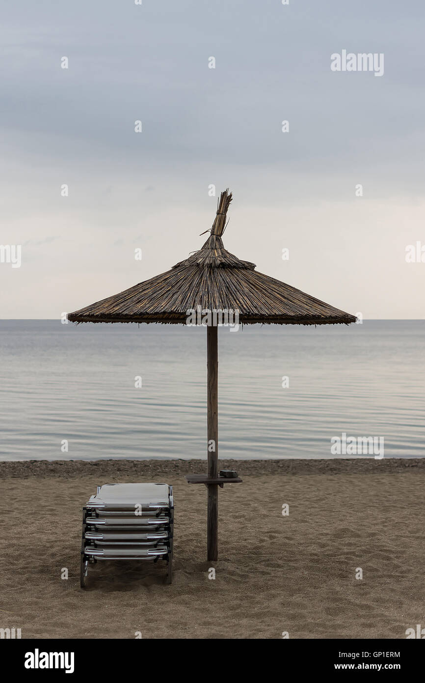 Reed-Sonnenschirm mit Liegestühlen am Sandstrand. Sonnenschirm und Liegebetten trübem Wetter und ruhige See. Stockfoto