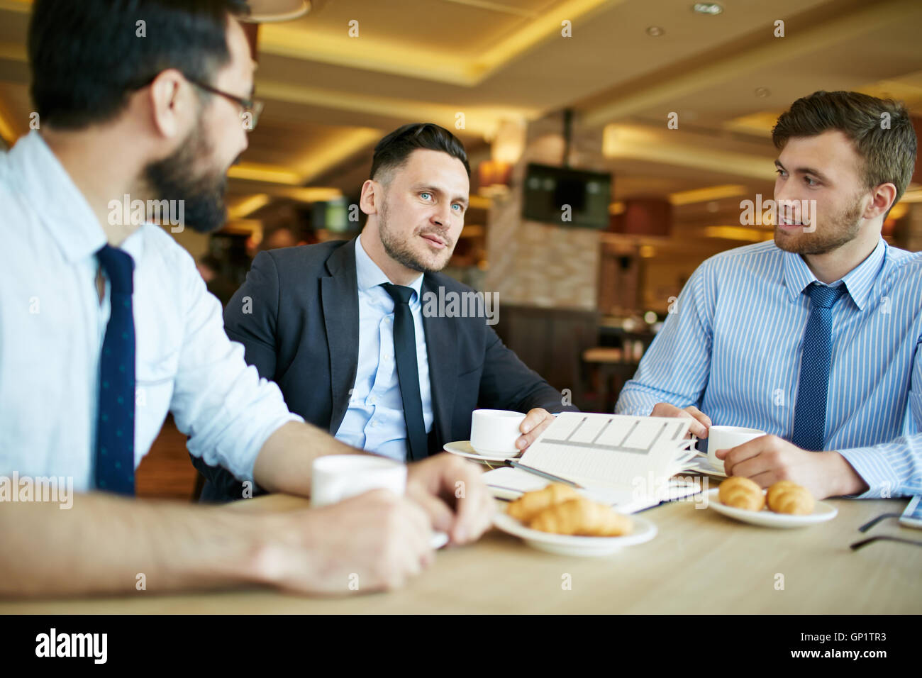 Drei entspannte formell gekleideten Geschäftsmänner auf zwanglose Geschäftstreffen im Café mit Kaffee mit Croissants und diskutieren wor Stockfoto