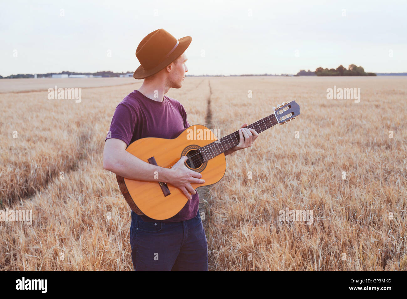 junger Mann im Sonnenuntergang, romantisches Liebeslied Gitarrespielen im Feld Stockfoto