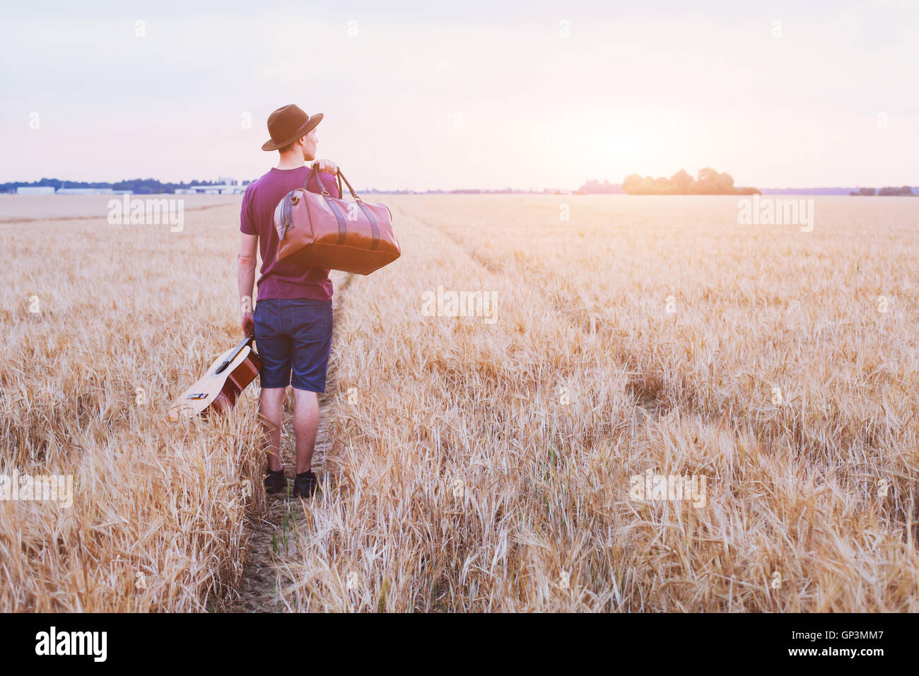 kleinen Sohn aus dem Haus, romantische Reise Hintergrund, Mann mit Gitarre und Straße Tasche Wandern bei Sonnenuntergang Feld Stockfoto