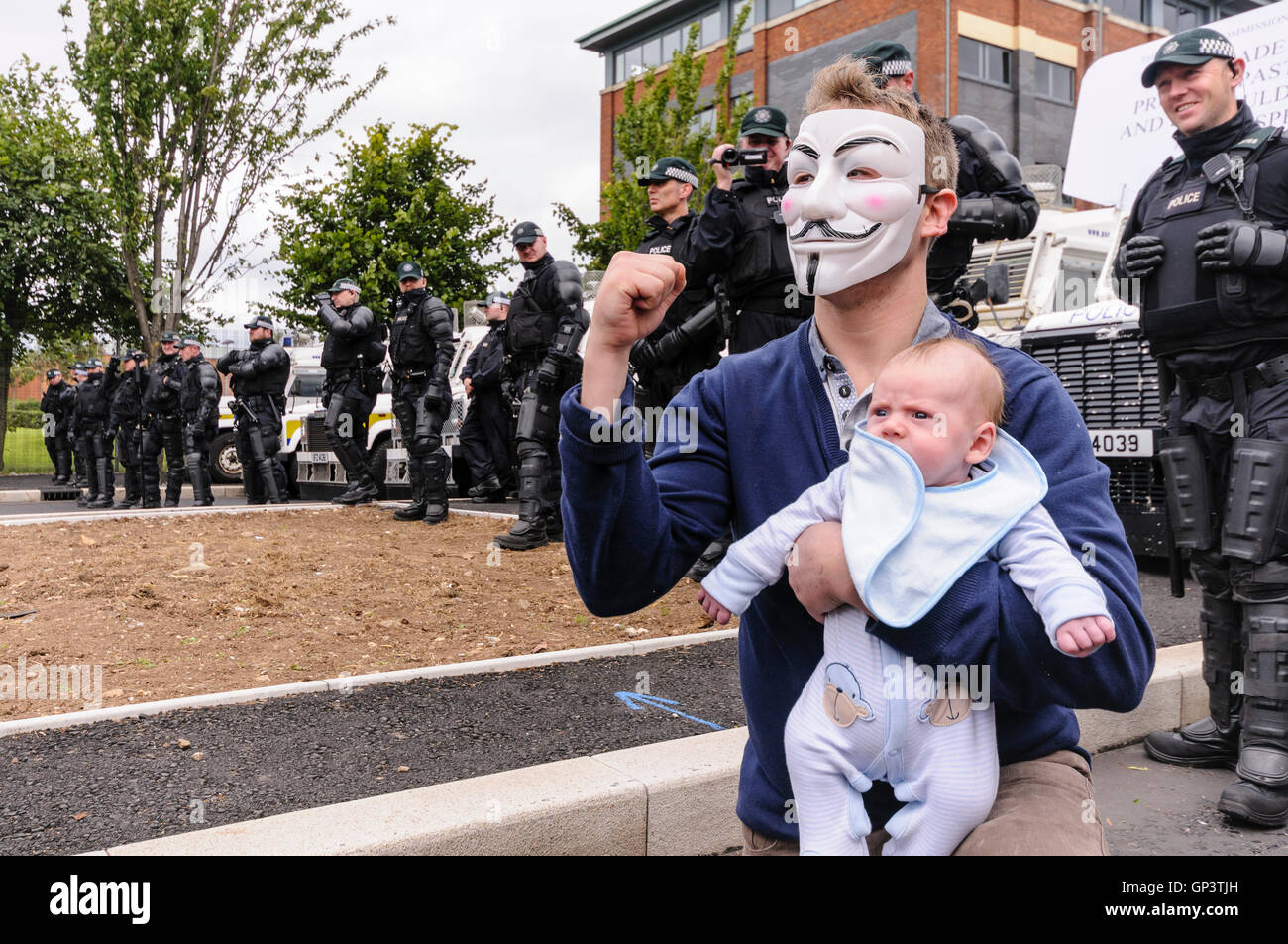 Ein Mann trägt einen 'Anonymous' Guy Fawkes-Maske, und hält ein Baby gibt  einen trotzigen Gruß vor einer Reihe von PSNI Polizisten Stockfotografie -  Alamy
