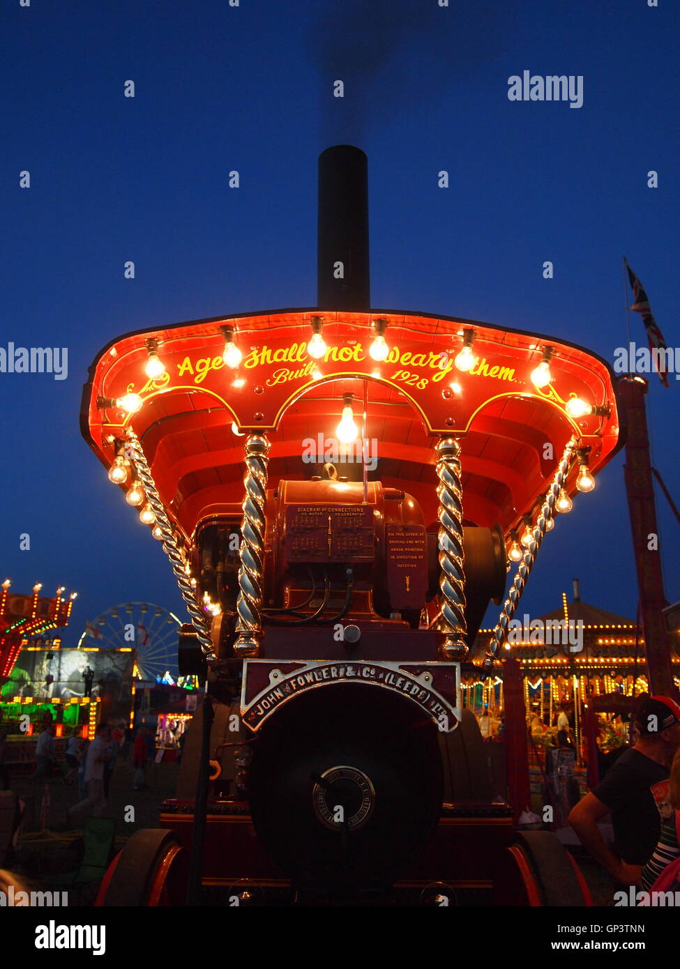 Dies ist die Vorderseite des einen Showmans Dampftraktor durch einen eigenen Generator und Glühbirnen, Kirmes im Hintergrund beleuchtet Stockfoto